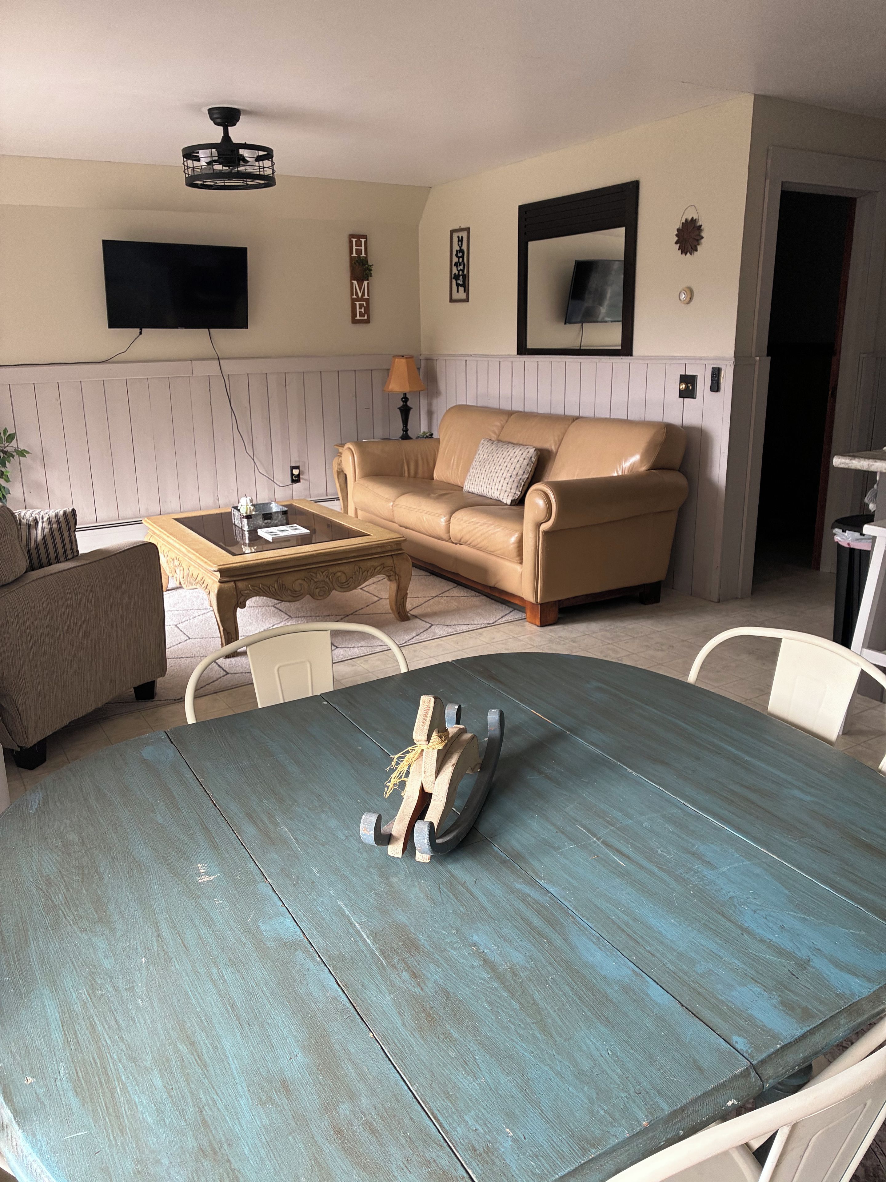 Una sala de estar con un sofá color beige, una mesa de centro y una mesa de comedor con una escultura decorativa de un caballo.