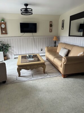 A living room with a sofa, coffee table, television, and decorative items. - Cozy Mountain View Retreat (Brighton)