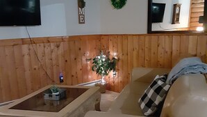 Ein Wohnzimmer mit beiger Couch, Couchtisch, Fernseher und einer Wandverkleidung aus Holz.