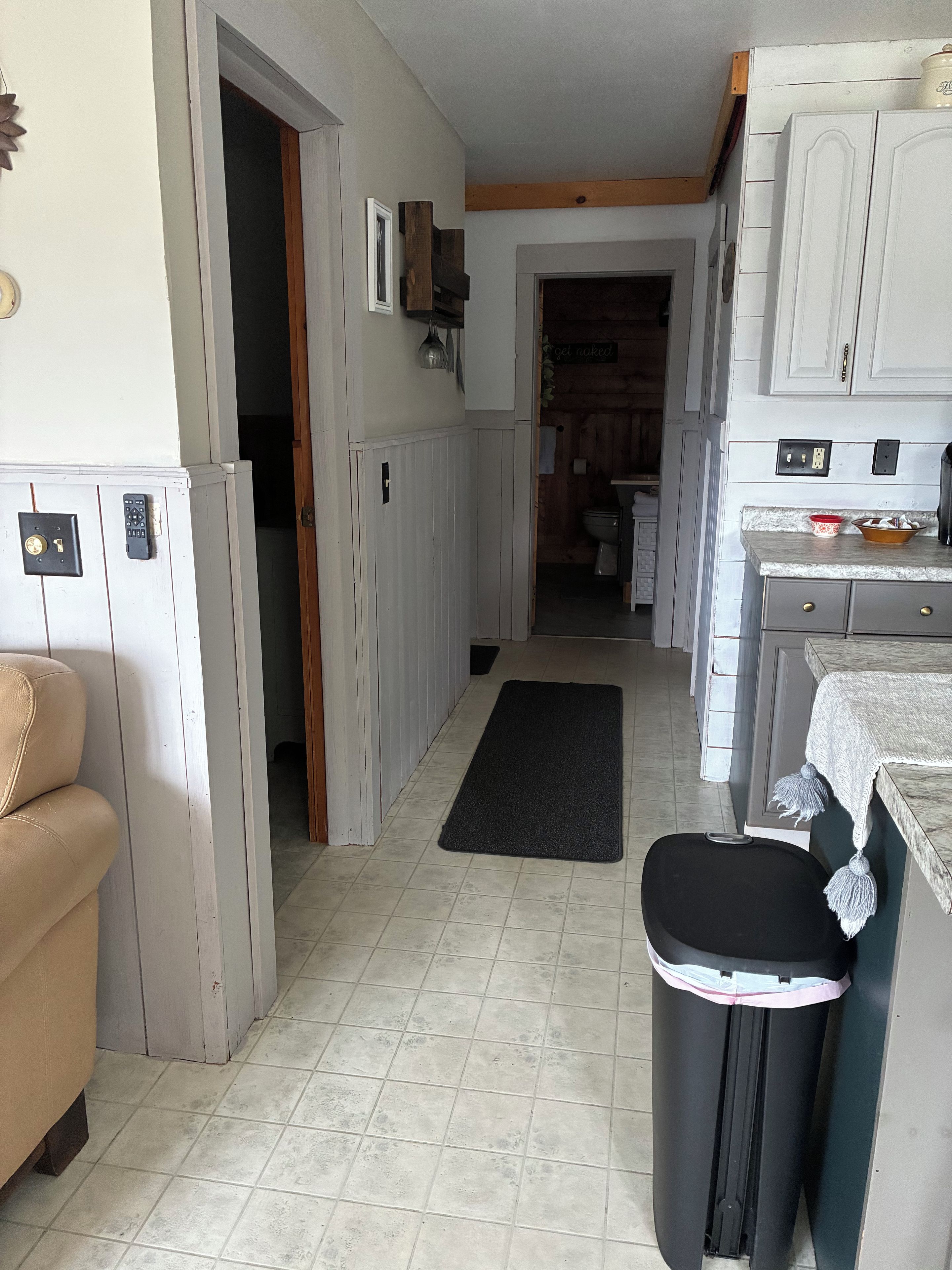 Una cocina con armarios blancos, un bote de basura negro y un tapete negro en el suelo.