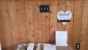 Ein Empfangstresen mit einer Wandpaneele aus Holz, einem 'Welcome'-Schild, einem Hinweis zum WLAN-Passwort und einem Bulletinboard mit einem Aushang.