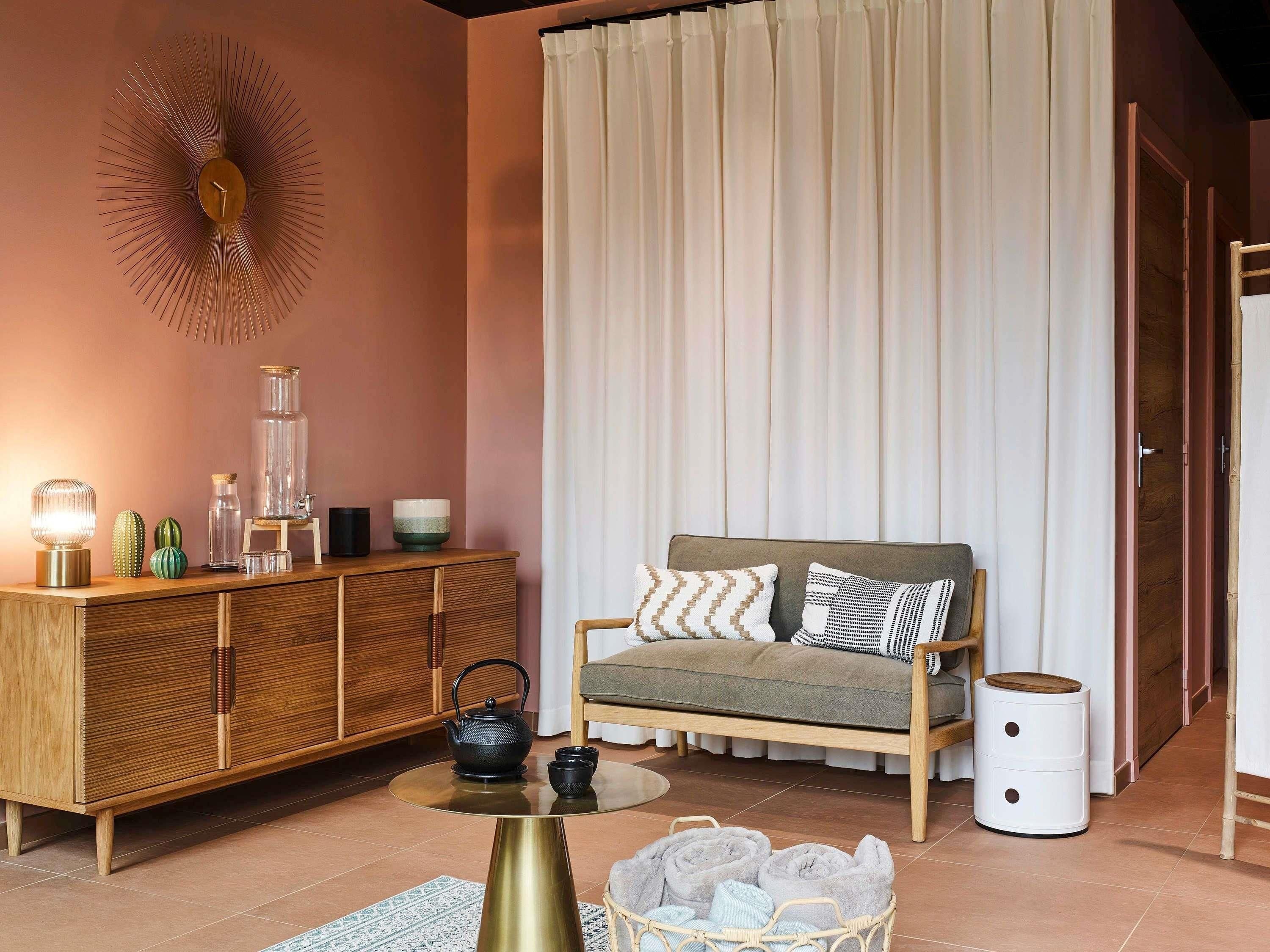 Ein gemütliches Wohnzimmer mit einer Couch, einer Holzkommode, einem Tisch mit Teekanne und einem dekorativen Wandbild.