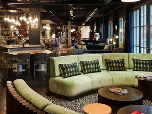 Un espacio lounge moderno con un sofá verde, mesas redondas y un bar al fondo.