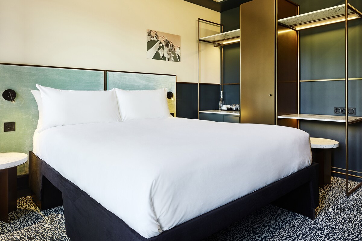 Una habitación de hotel moderna con una cama grande, mesitas de noche, un espejo y un pequeño escritorio con una silla.