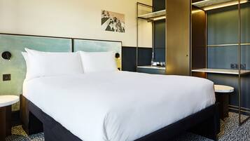 A modern hotel room with a large bed, bedside tables, a mirror, and a small desk with a chair.