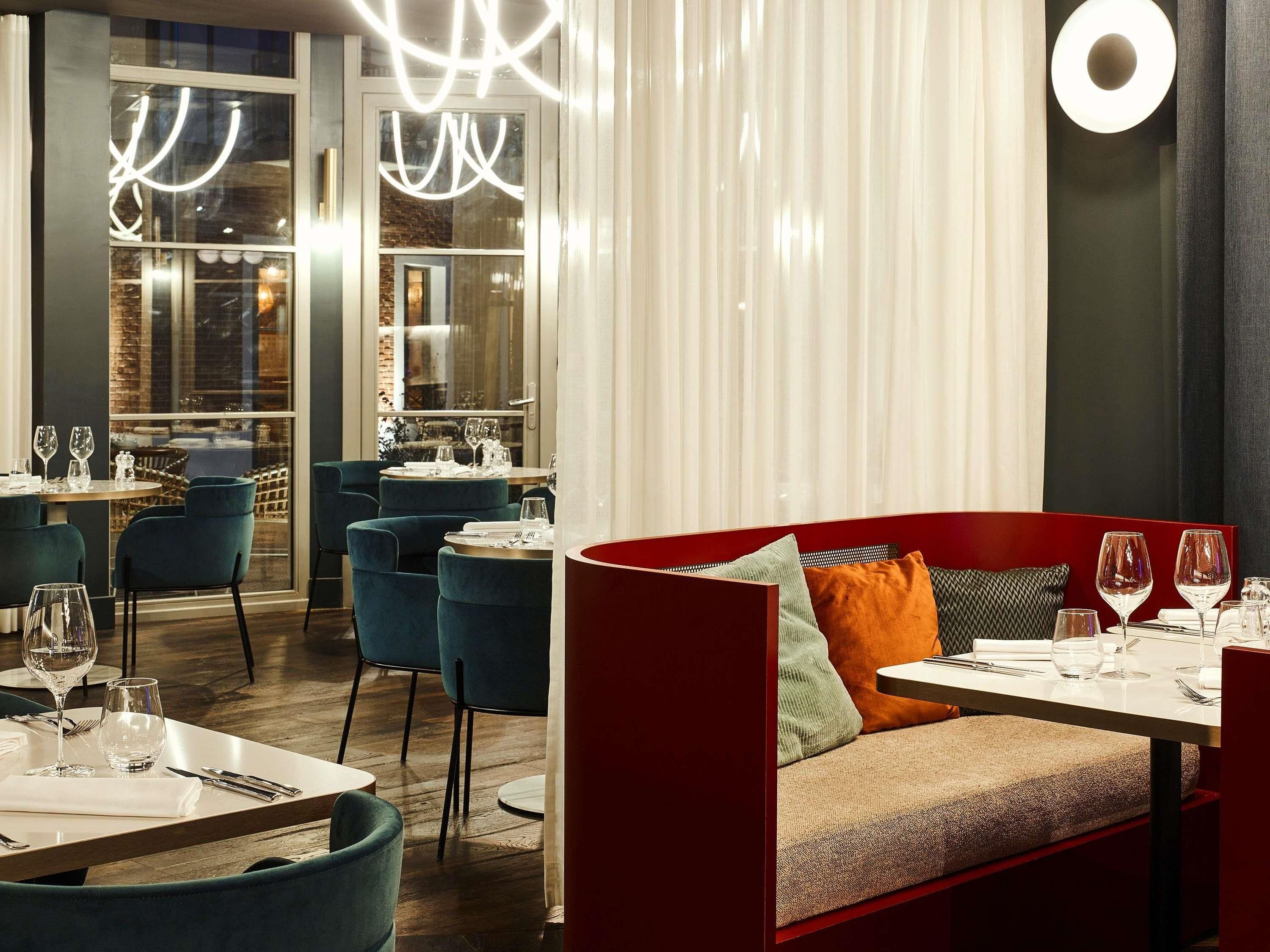 A restaurant interior with round tables, blue chairs, a red sofa, and a view through large windows.