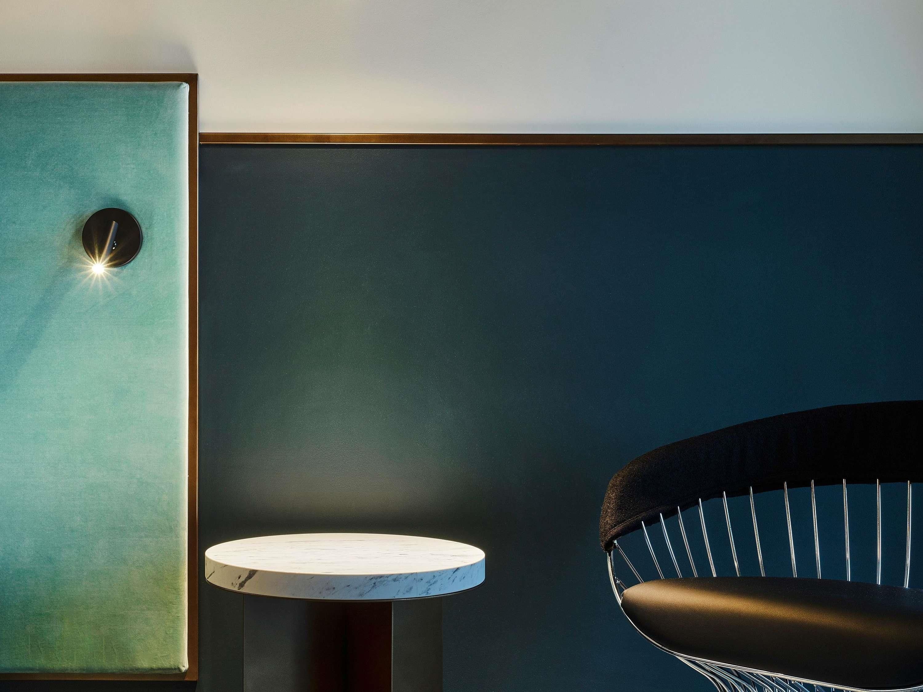 A room with a teal-colored cabinet, a round table with a marble top, and a black chair with a woven backrest.