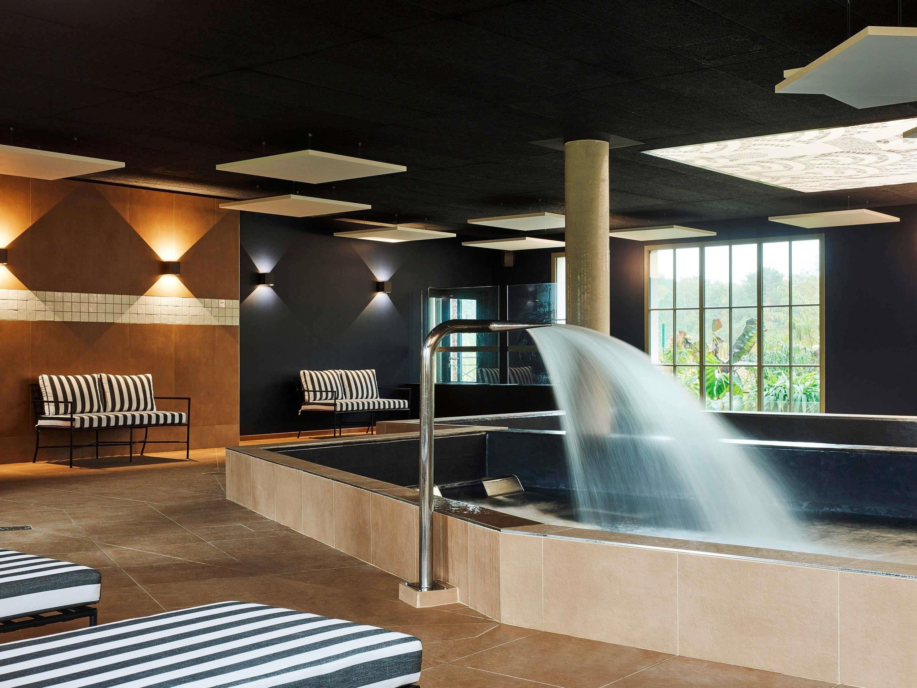 Un espace spa comprenant un bain à remous, deux chaises longues à rayures et une cascade décorative.