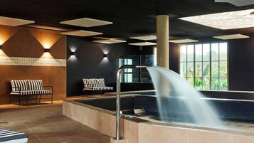 Un espace spa comprenant un bain à remous, deux chaises longues à rayures et une cascade décorative.