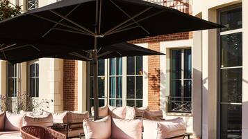 Un espace extérieur aménagé avec des sièges, comprenant un grand parasol, des canapés confortables et des fauteuils en osier.