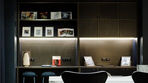 Un moderno área de bar con encimeras de mármol, taburetes negros y una estantería con libros y fotos enmarcadas.