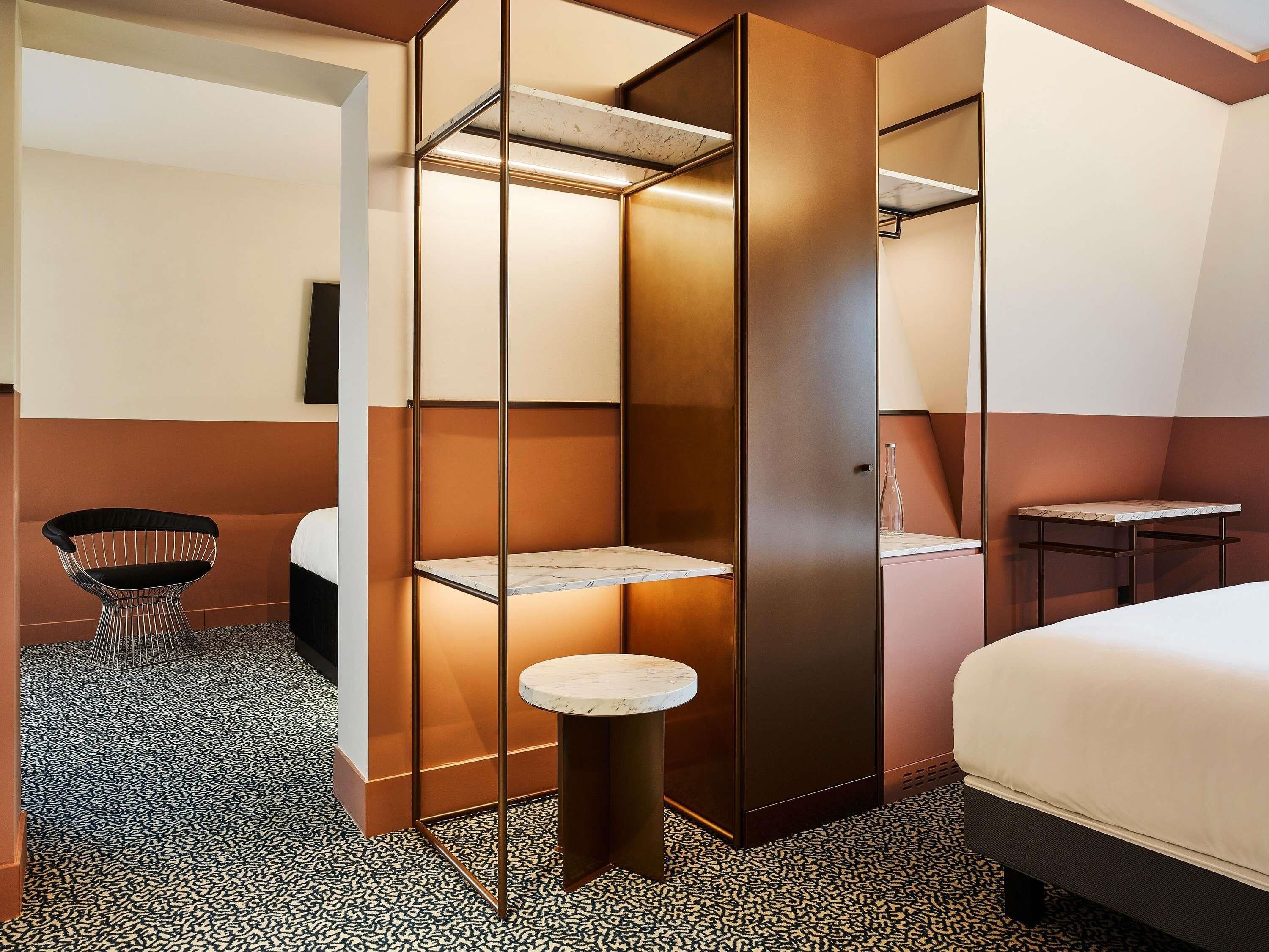 Una habitación de hotel con cama, una mesita redonda pequeña, una silla, un armario y una estantería.