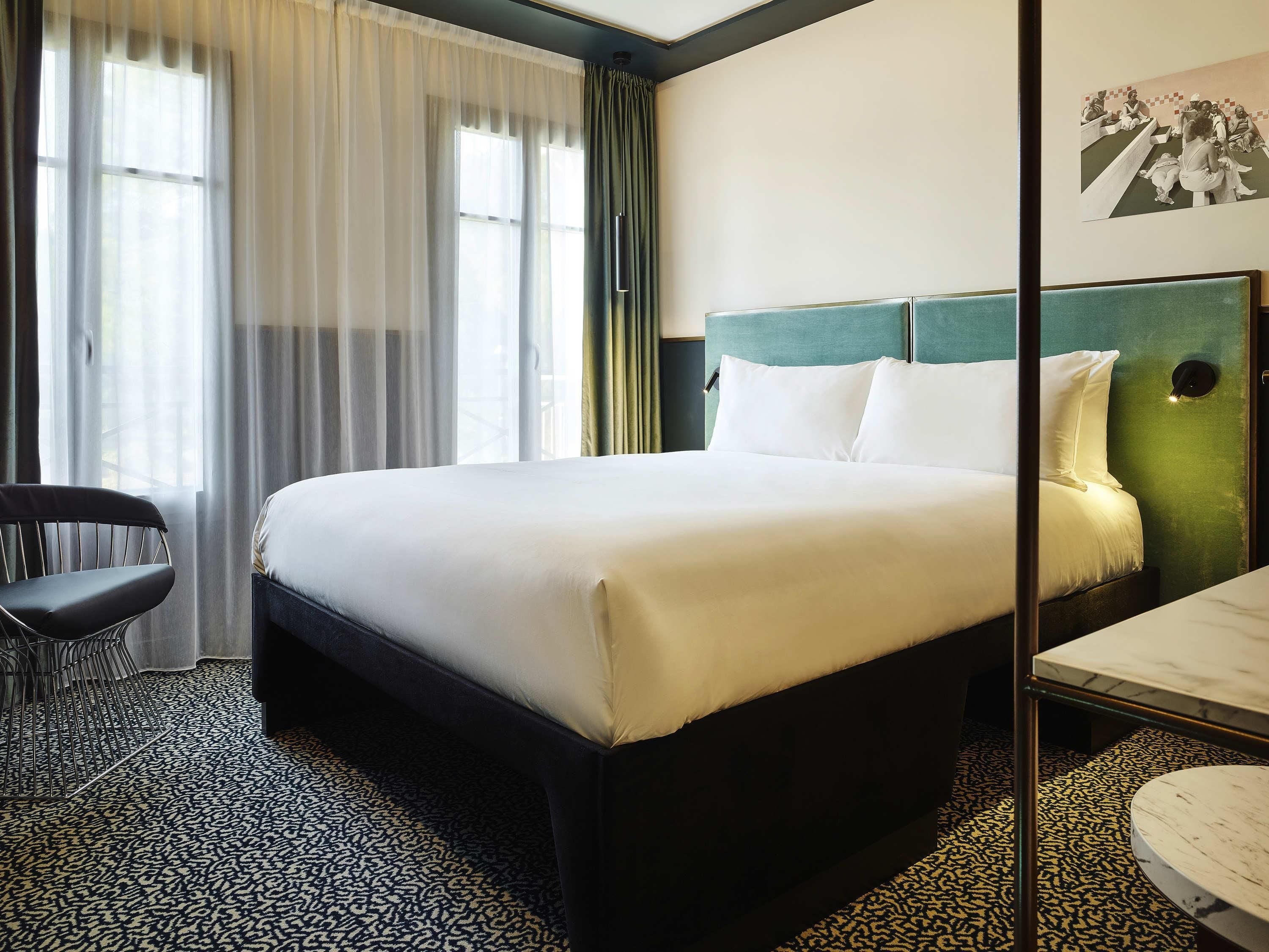 A hotel room with a large bed, a desk, a chair, and a patterned carpet.
