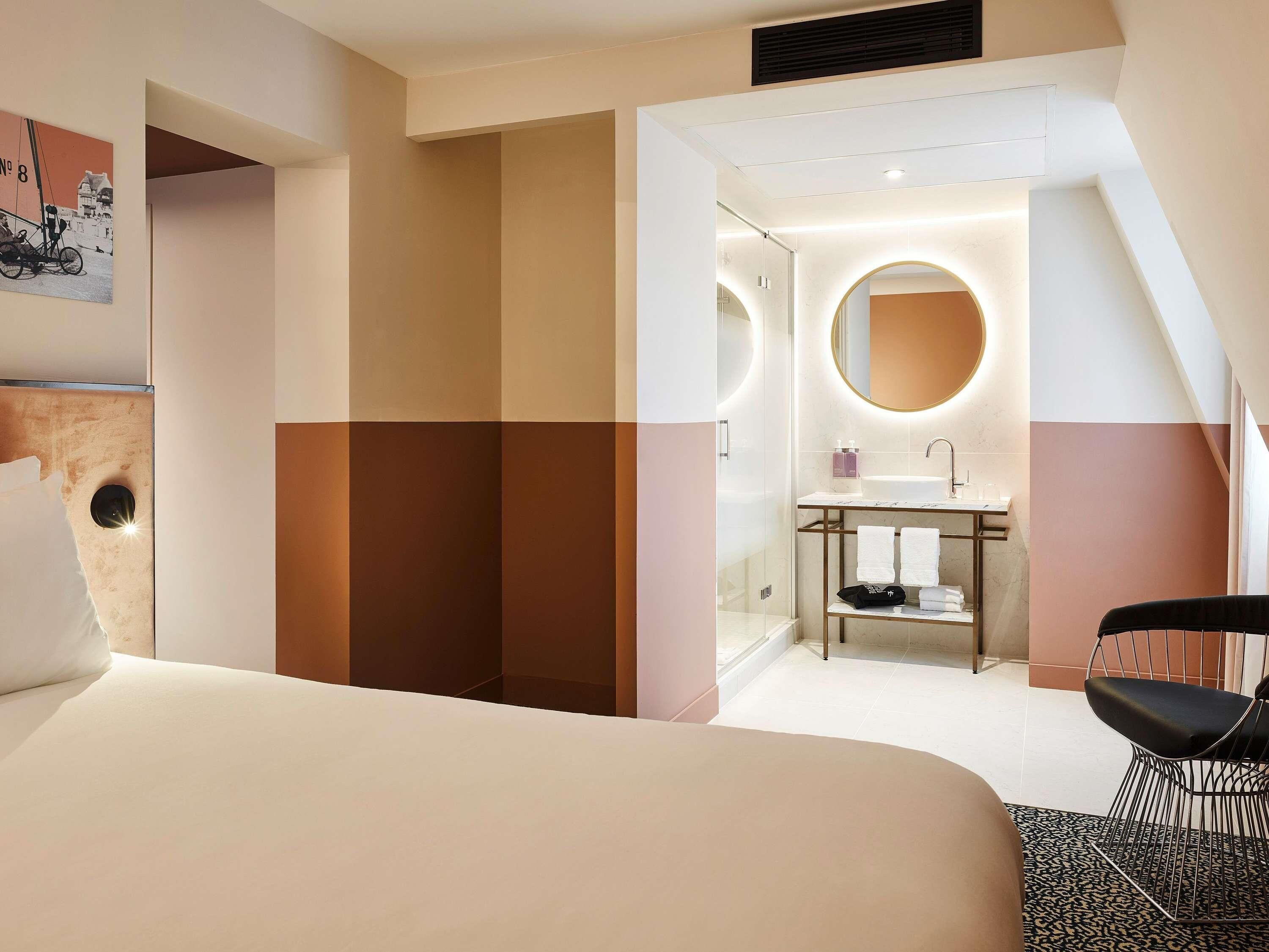 A hotel room with a bed, a bathroom with a sink and mirror, and a chair.