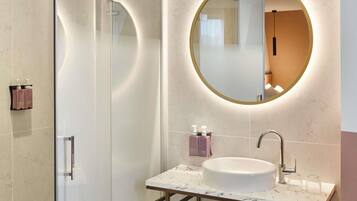 Un baño moderno con cabina de ducha de vidrio, espejo redondo, lavabo de mármol y toallero.