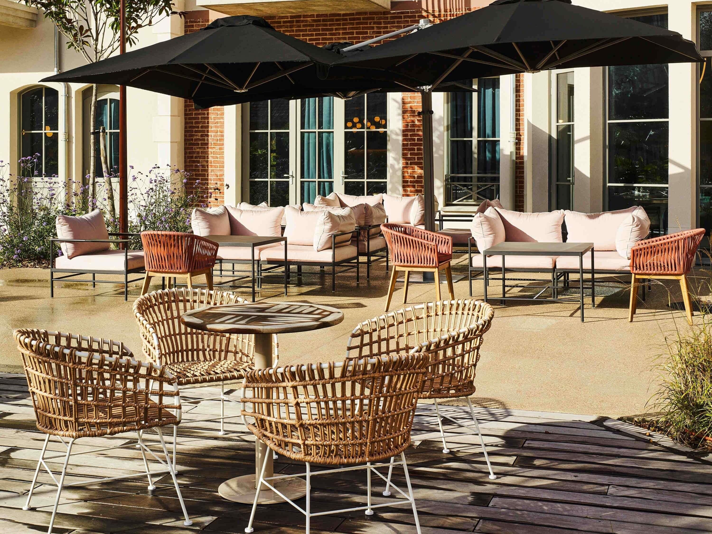 An outdoor patio with wicker furniture, large windows, and a brick building in the background.