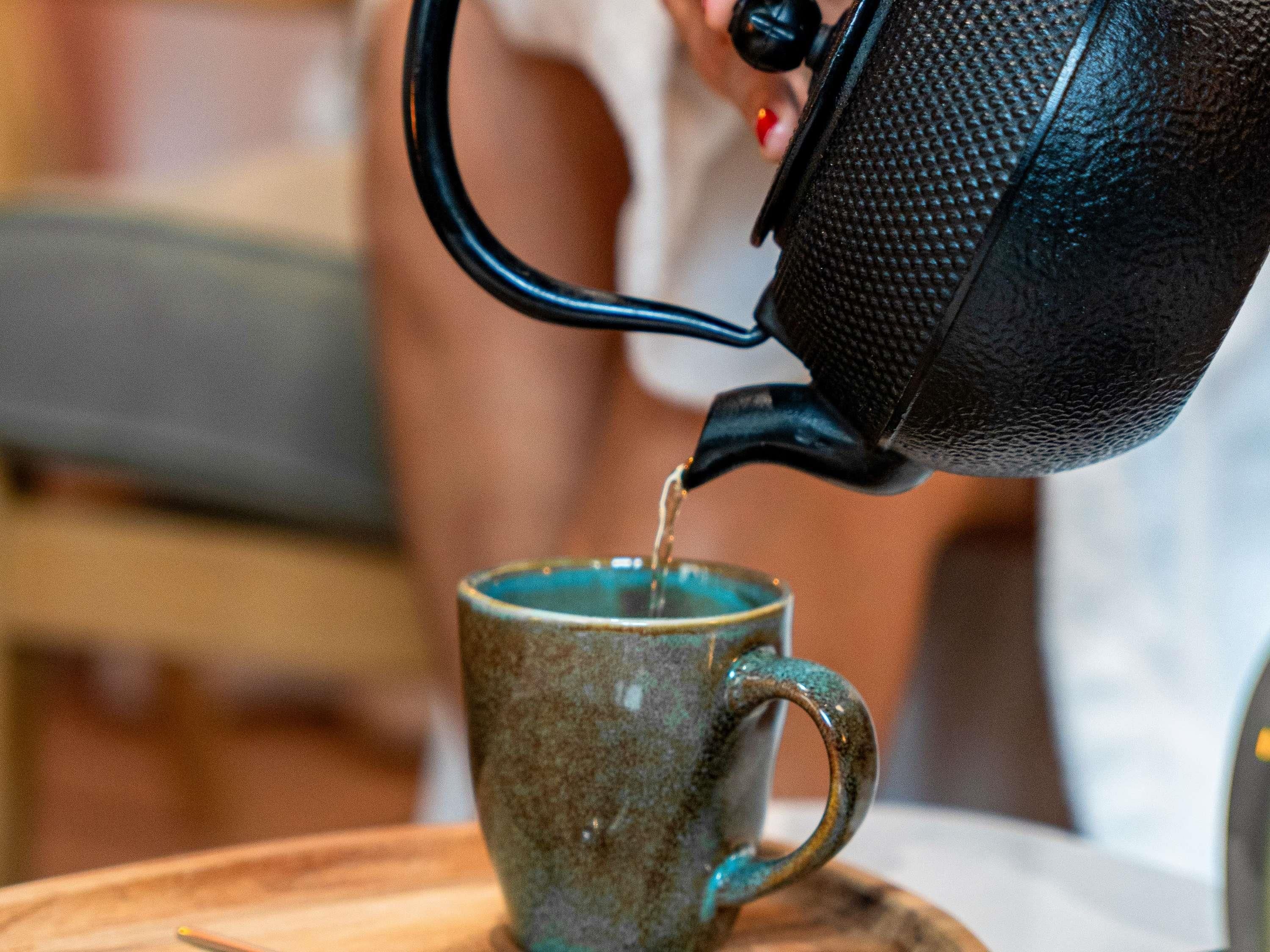 A person pouring liquid from a kettle into a mug.
