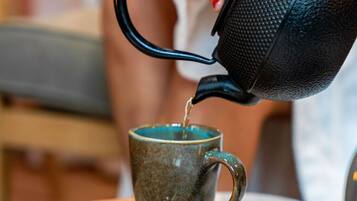 A person pouring liquid from a kettle into a mug.