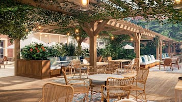 Un espace extérieur aménagé en terrasse, avec des meubles en osier, une pergola en bois et des guirlandes lumineuses.
