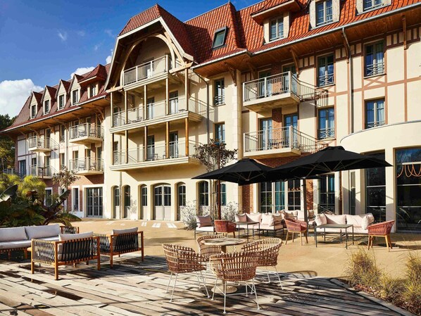 Un hotel de varios pisos con balcones, mobiliario exterior y un patio.