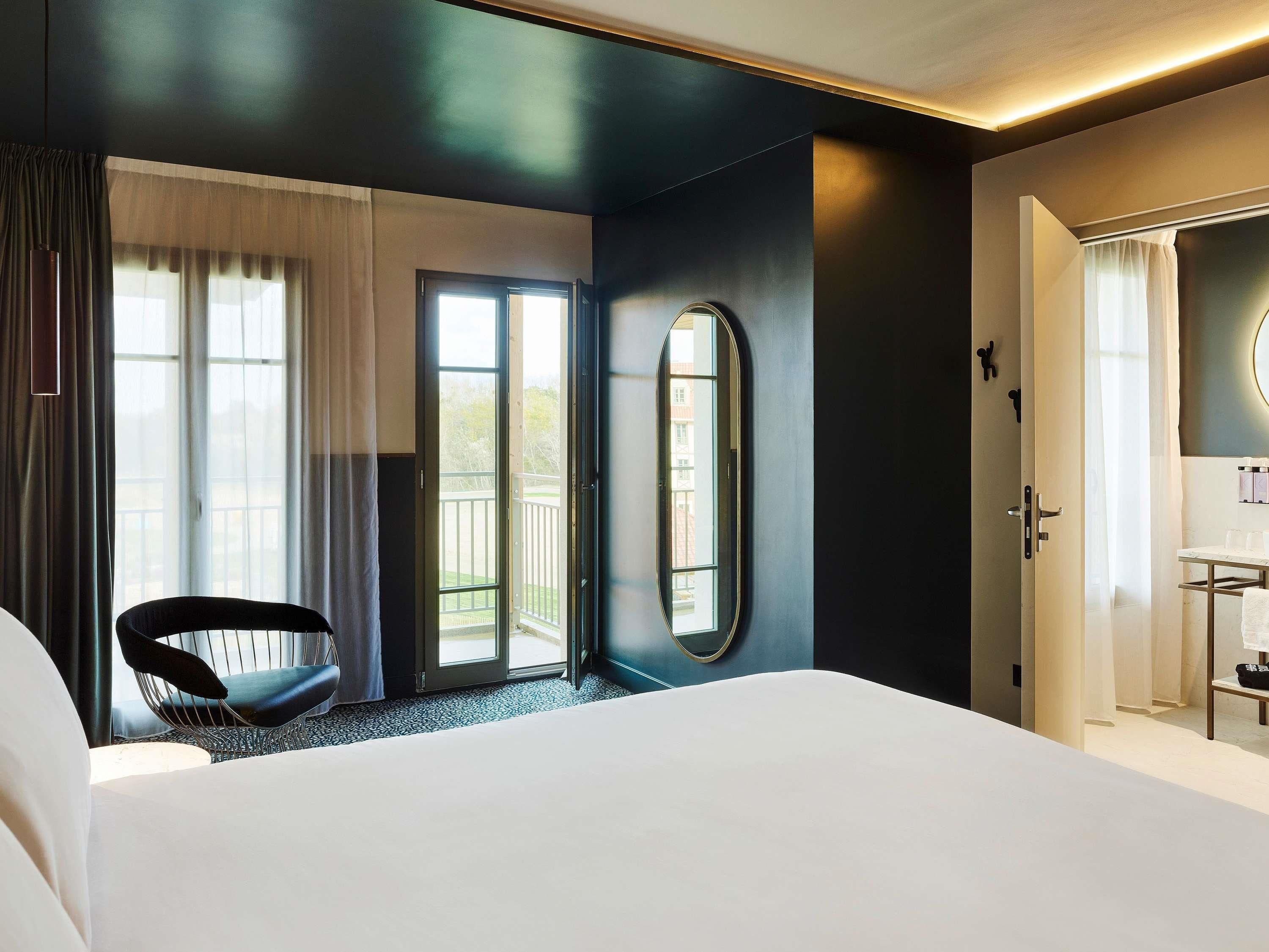 Ein Hotelzimmer mit Bett, Stuhl, einer Tür und Blick ins Freie.