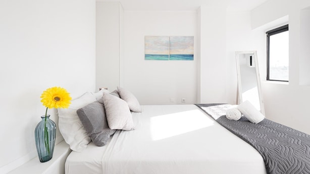 Ein modernes Schlafzimmer mit Bett, Kissen, einer Vase mit Blume, einem Gemälde und einem Fenster.