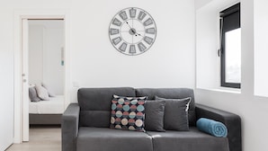 Ein modernes Wohnzimmer mit einem grauen Sofa, gemusterten Kissen und einer großen Wanduhr.