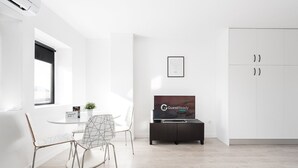 Ein modernes, minimalistisches Zimmer mit einem Bett, einem Fernseher, einem Schreibtisch und einem Stuhl.