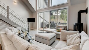 A modern living room with a staircase, a fireplace, and a large sliding glass door leading to an outdoor patio.
