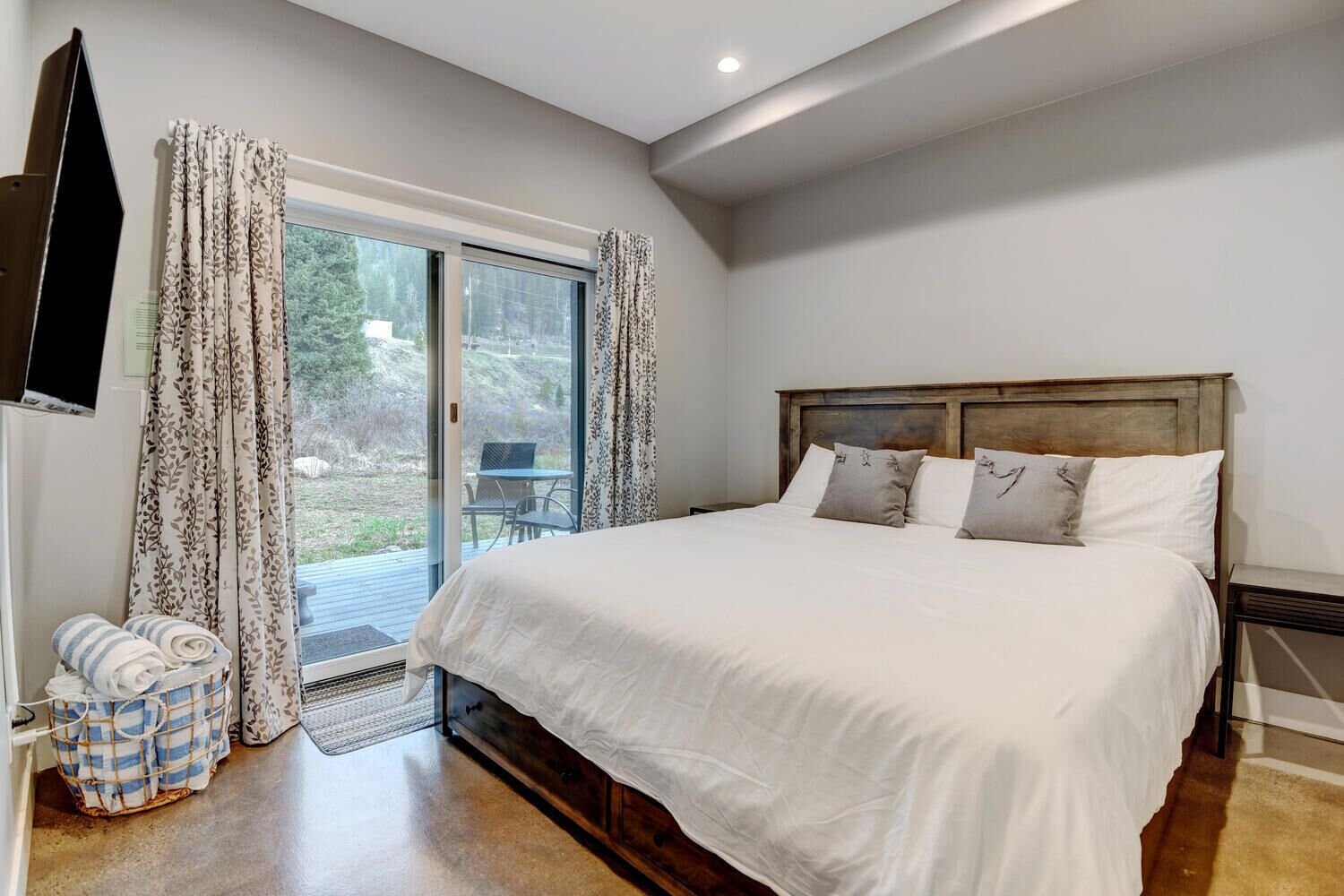 Een slaapkamer met een groot bed, een aan de muur bevestigde televisie en een schuifdeur naar een buitenruimte.