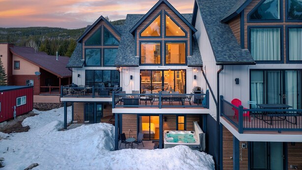 A modern multi-story house with large windows, a balcony, and a hot tub.