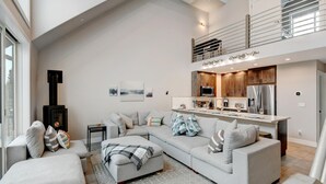 A modern living room with a sectional sofa, a fireplace, and a kitchen with wooden cabinets and stainless steel appliances.