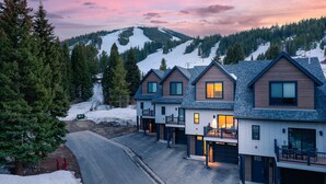 A row of modern, two-story houses with attached garages, set against a backdrop of snow-covered mountains and a twilight sky.