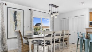 A dining area with a wooden table and chairs, a hanging light fixture, and a view of the outside. - Spring Break Ready! Pool | Game Room | Sleeps 21 (Gulf Breeze)