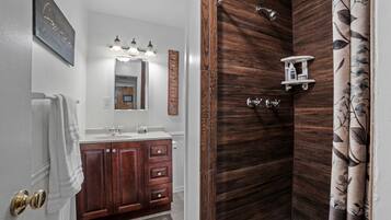 A bathroom with a wooden vanity, a mirror with lights, a shower with a wooden door, and a towel rack.