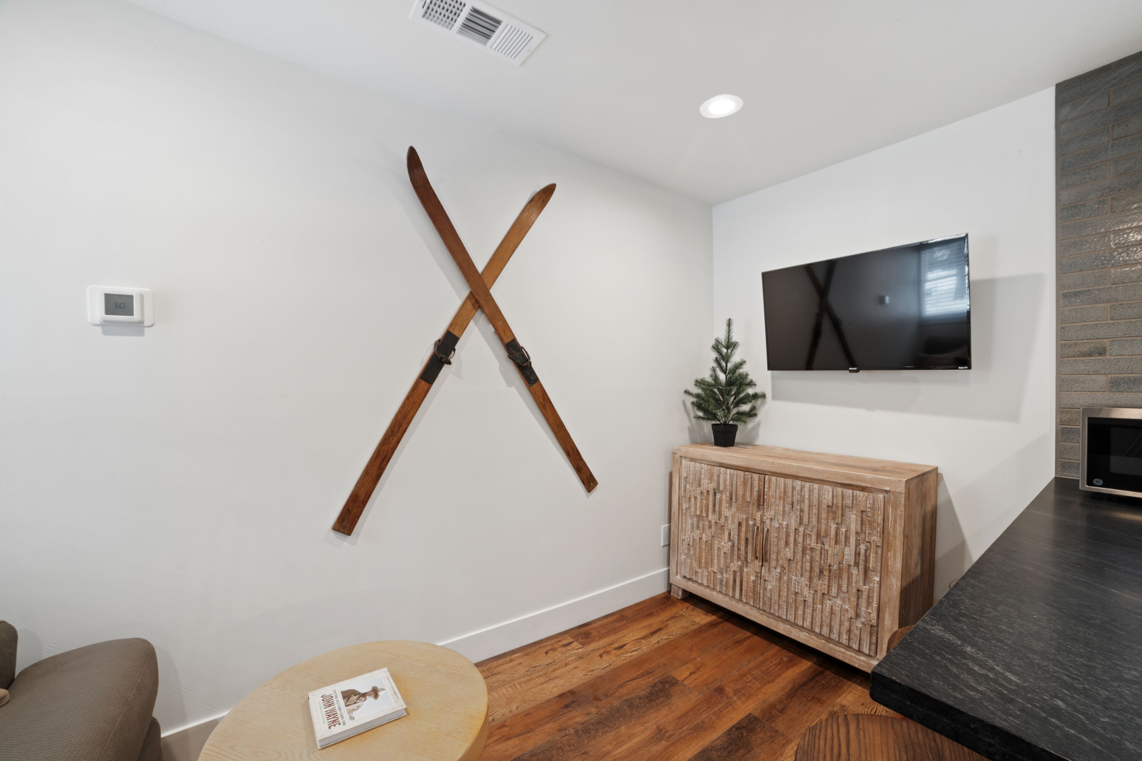 A modern living room with a wooden X-shaped wall decoration, a flat-screen TV, a wooden cabinet, and a round wooden table.