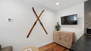 A modern living room with a wooden X-shaped wall decoration, a flat-screen TV, a wooden cabinet, and a round wooden table.