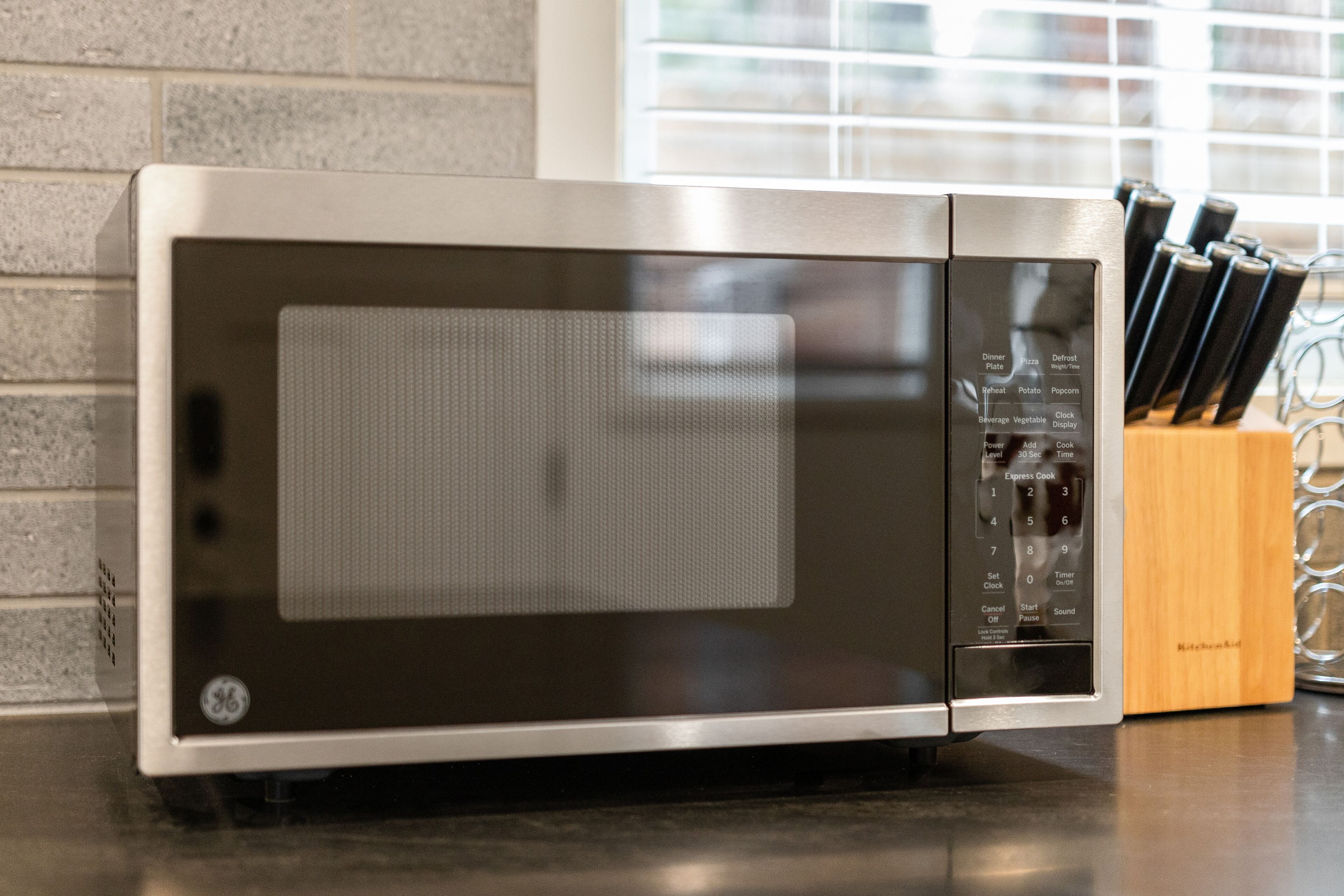 A kitchen with a microwave, a knife block, and a brick wall.