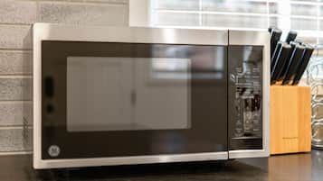 A kitchen with a microwave, a knife block, and a brick wall.