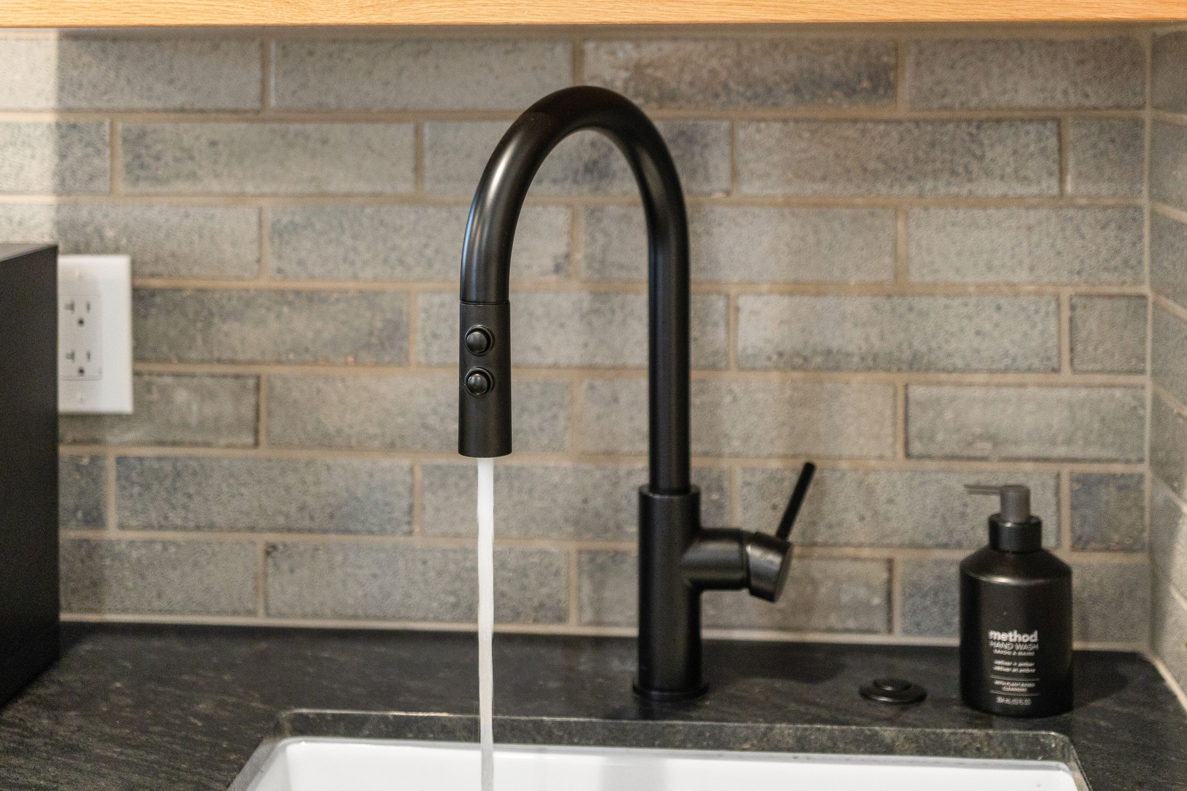 A kitchen sink with a black faucet and a bottle of Method hand wash soap on the counter.