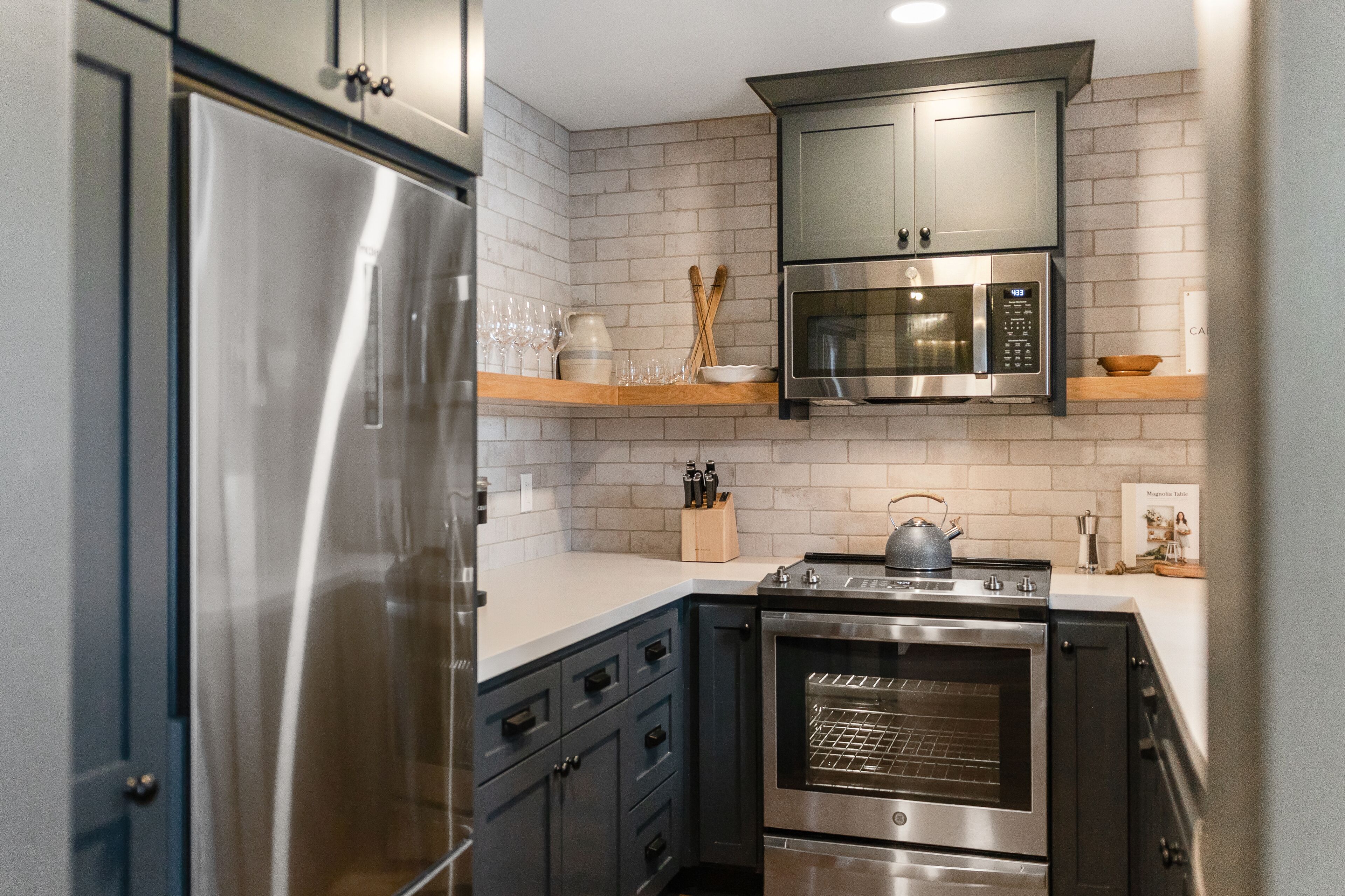 A kitchen with stainless steel appliances, wooden shelves, and a tiled backsplash.