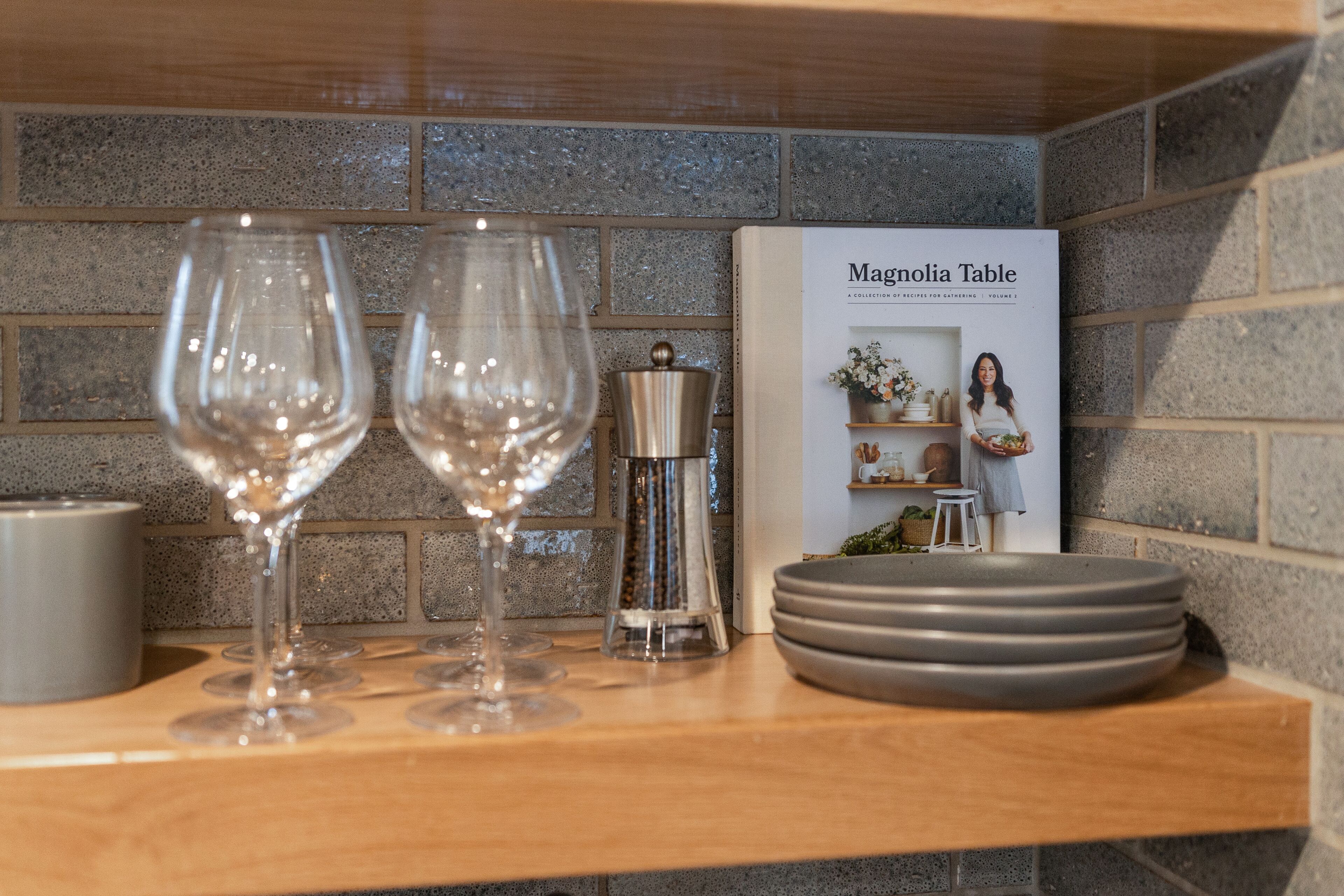 A kitchen counter with two wine glasses, a salt and pepper shaker, and a cookbook titled 'Magnolia Table'.