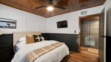 Un dormitorio con una cama, ventilador de techo, televisión, puerta y un cuadro en la pared.