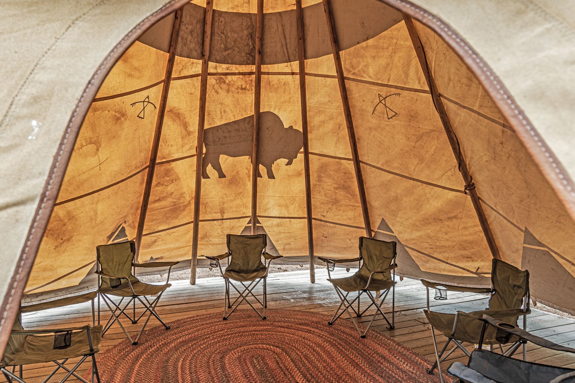 A tent with a wooden interior, a central buffalo silhouette, and four folding chairs arranged around a central table.