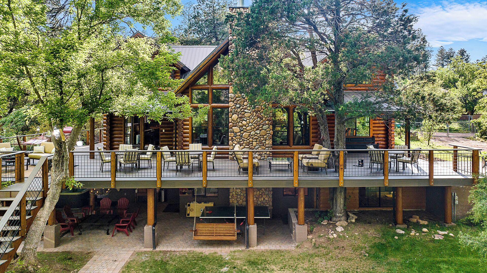 A log cabin with a deck, outdoor seating, and a stone wall.