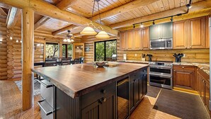 L’intérieur d’une cabane en rondins présente une grande table à manger en bois, un coin cuisine doté d’appareils électroménagers en acier inoxydable et un plafond en bois.