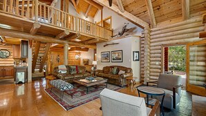 L’intérieur de cette vaste cabane en rondins est doté d’un plafond haut, d’un salon confortable avec des canapés en cuir, d’une table à manger et d’un escalier menant à un étage supérieur.