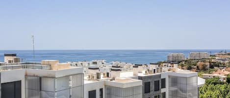 A coastal residential area with modern buildings, some with balconies, and a clear view of the sea.