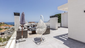 Eine Dachterrasse mit Hängesessel, Sonnenschirm und Korbmöbeln.
