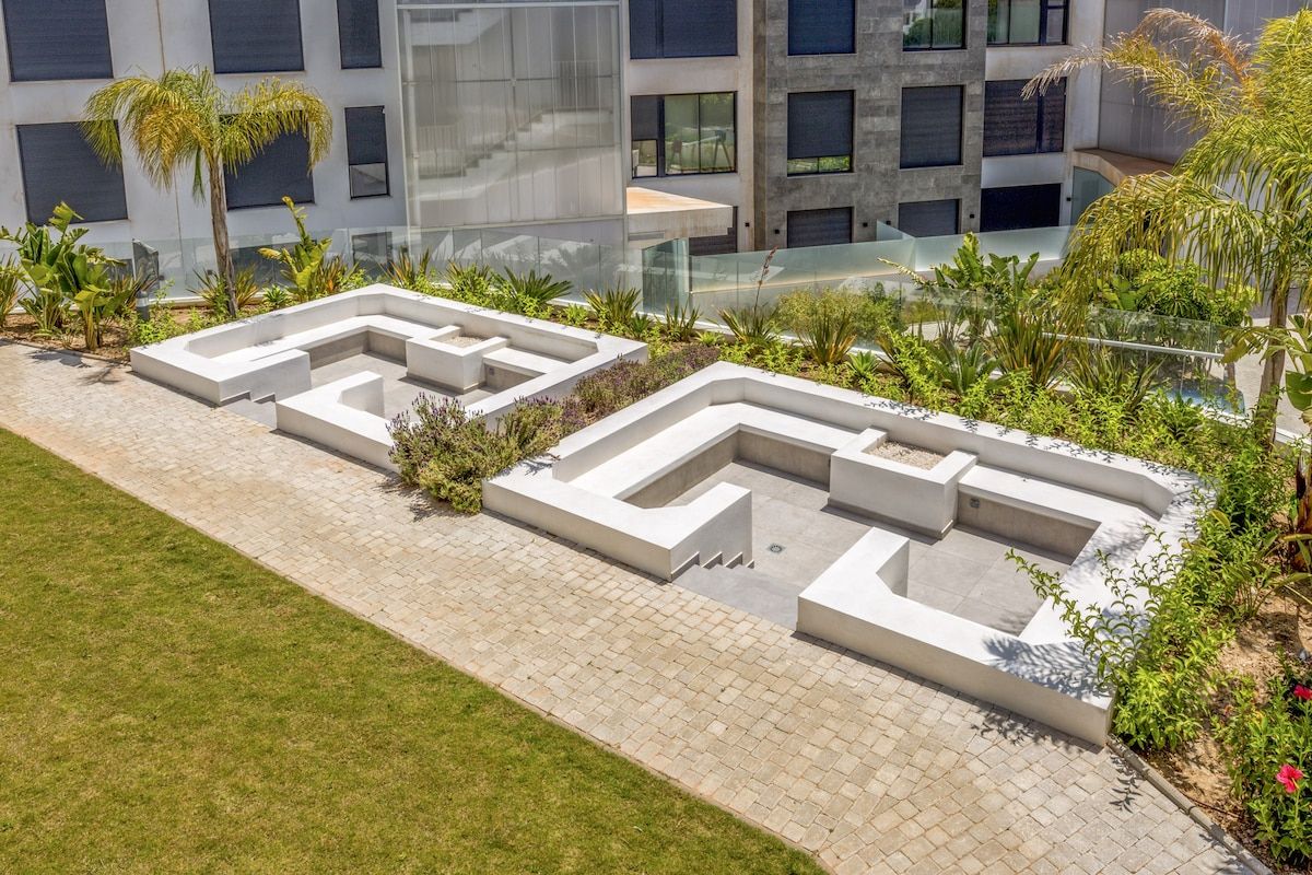 Ein angelegter Garten mit geometrischen Wegen und modernen Gebäuden im Hintergrund.